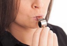 Person blowing a silver whistle close-up.