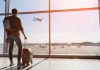 Traveler with luggage watches airplane take off at airport.